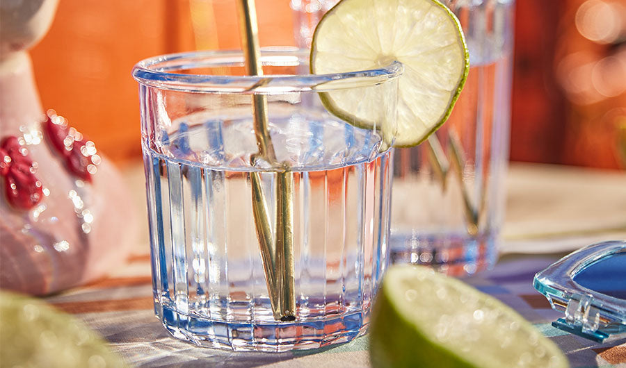 Blaues Cocktailglas mit Limettenscheibe und goldenem Strohhalm