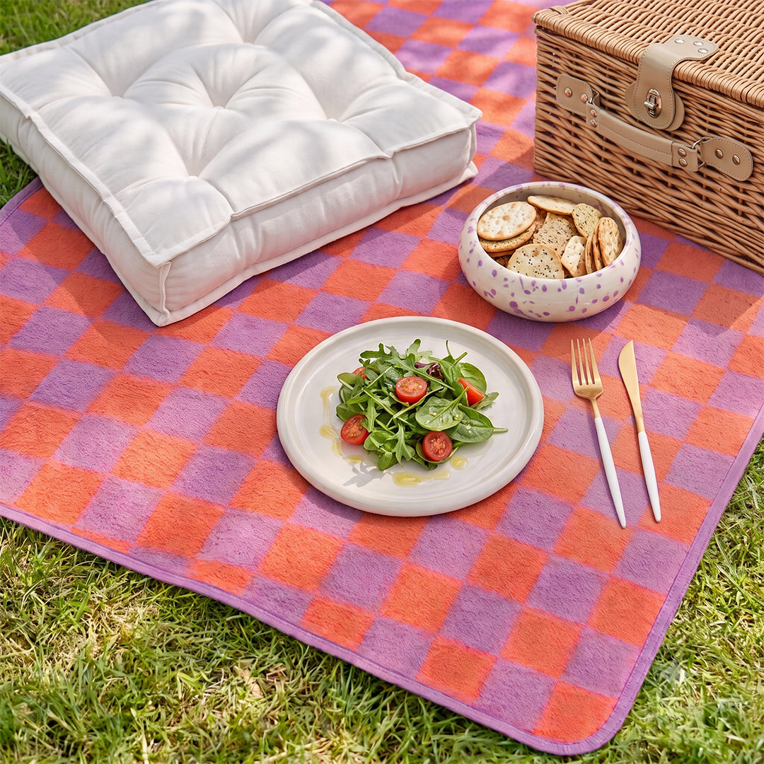Geblümte Picknickdecke auf Wiese mit Weidenkorb und Kissen
