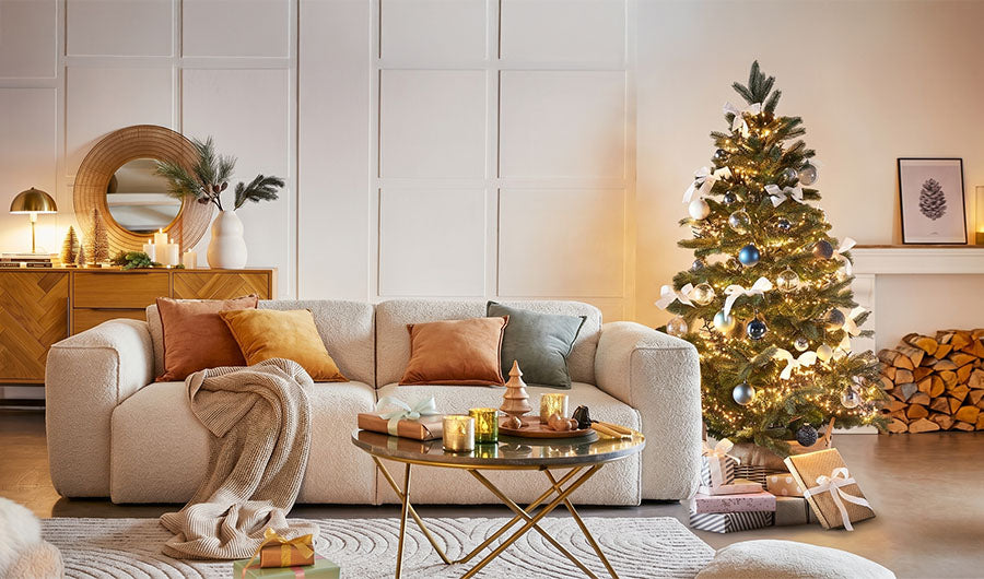 Geschmückter Weihnachtsbaum neben cremefarbenem Sofa im festlichen Wohnzimmer