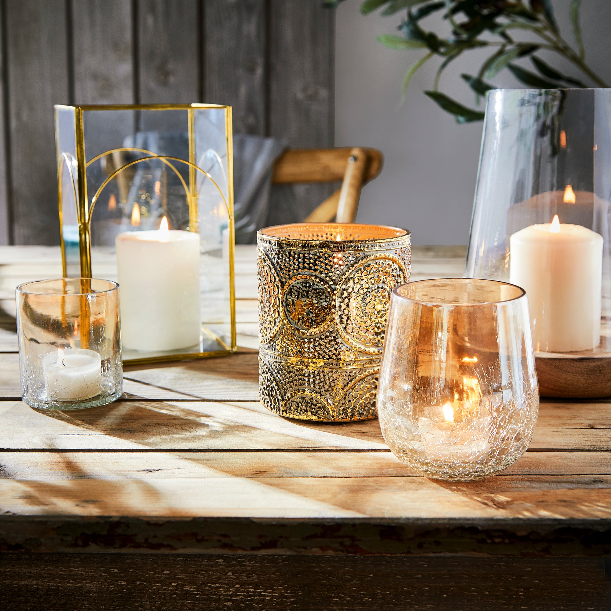 Goldene und gläserne Windlichter mit Kerzen auf Holztisch