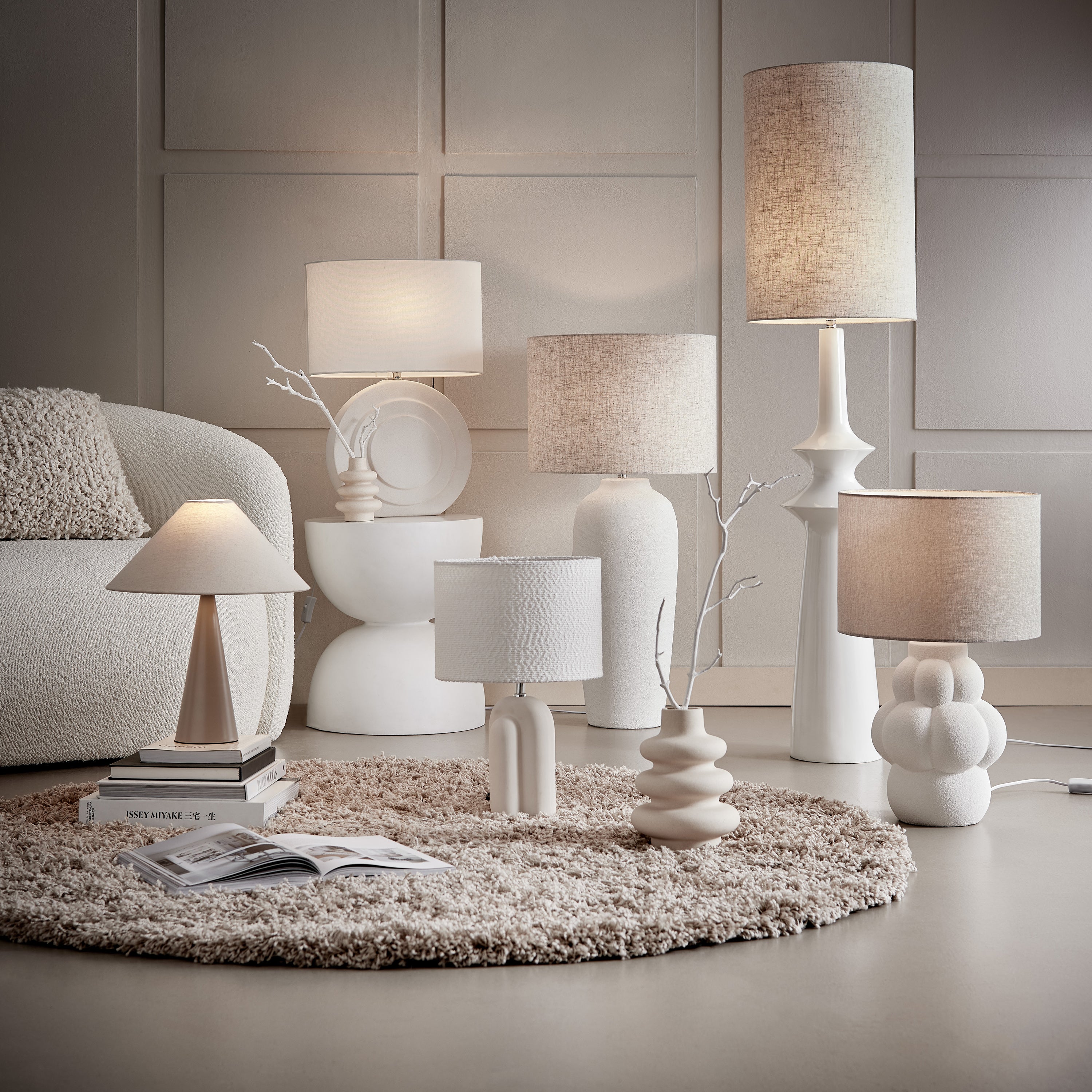 Moderne Tischlampen in Weiß und Beige: Verschiedene Größen und organische Formen stilvoll arrangiert auf einem beigen Teppich vor einer hellen Wand im Wohnzimmer.
